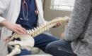 A spine doctor discussing holistic solutions for living with back pain with a patient in his office, using a model of the spine.