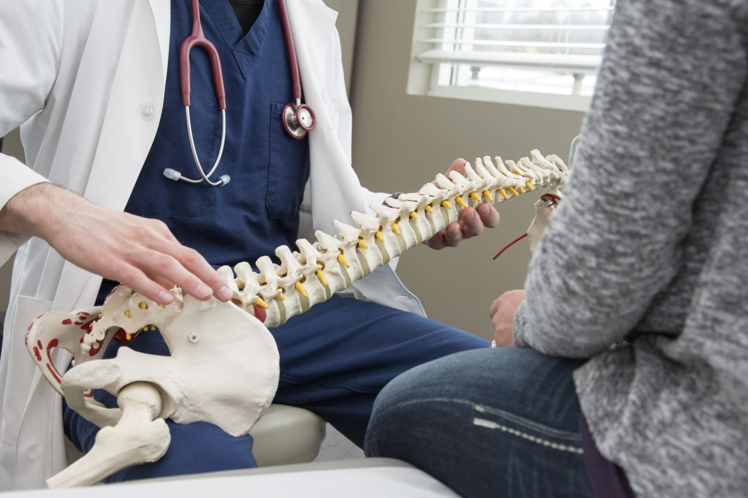 A spine doctor discussing holistic solutions for living with back pain with a patient in his office, using a model of the spine.