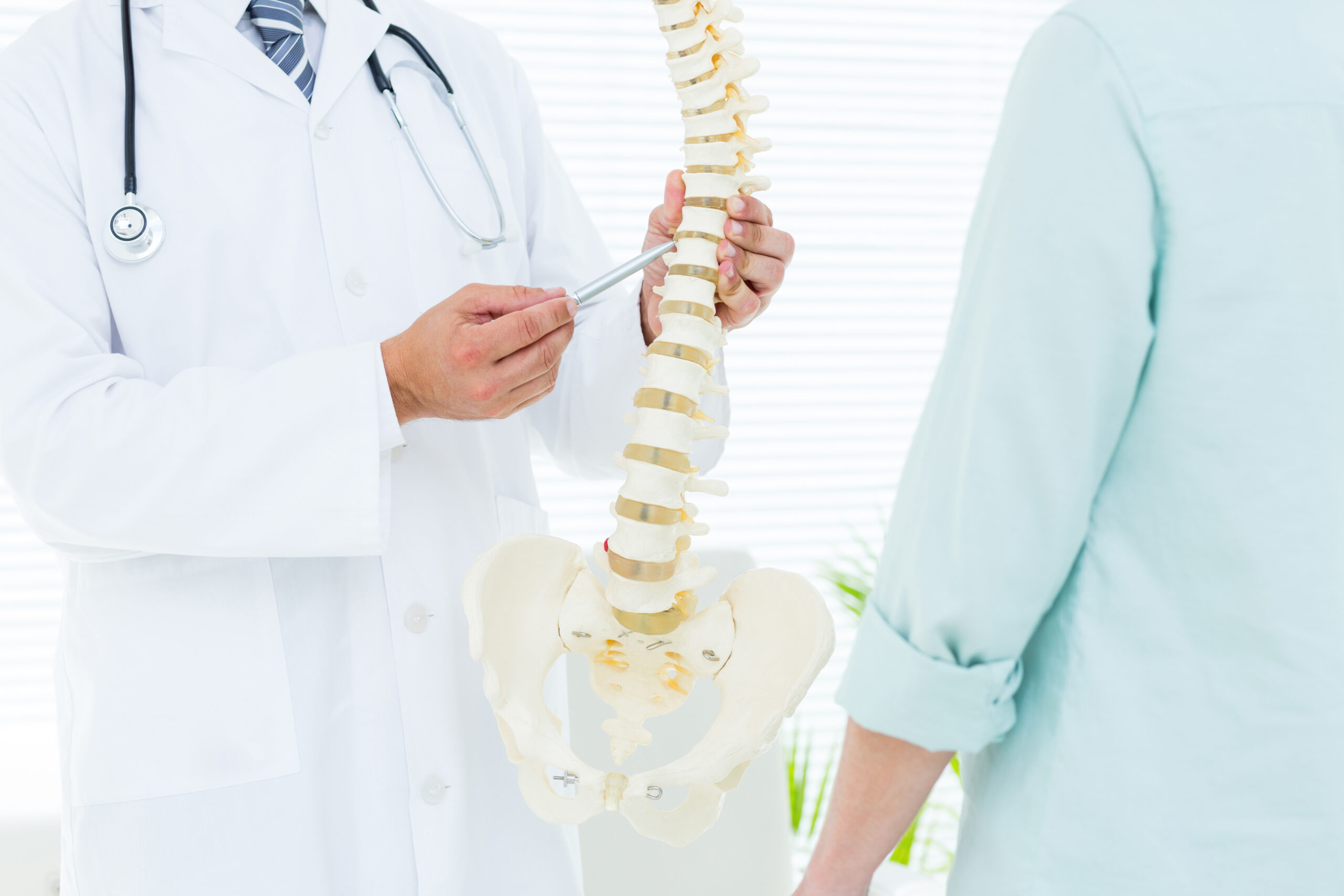 A spine doctor discussing back pain relief options with a patient, using a model of the human spine.
