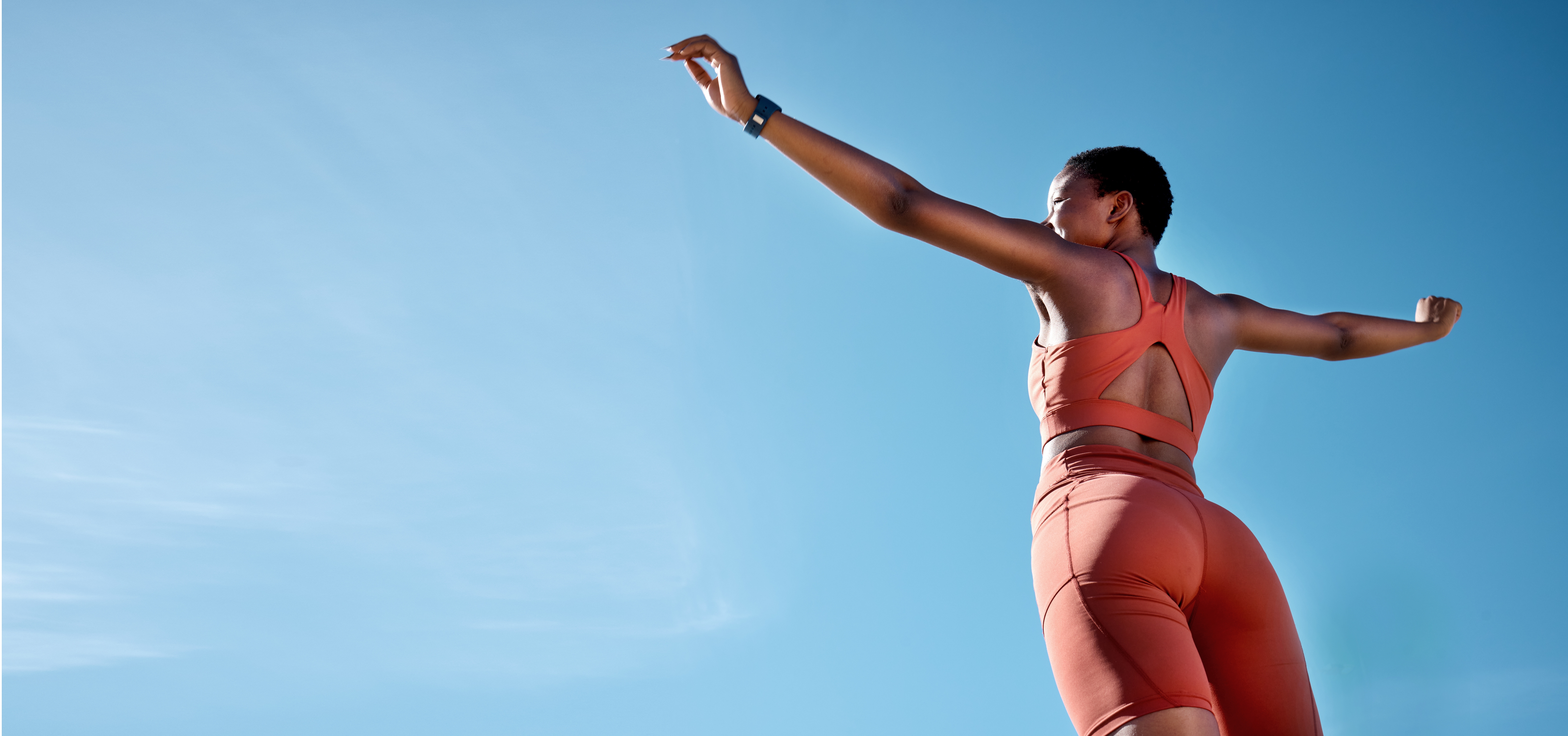 An adult woman wearing an exercise outfit, and having outstretched arms, considers her options for holistic solutions for living with back pain.