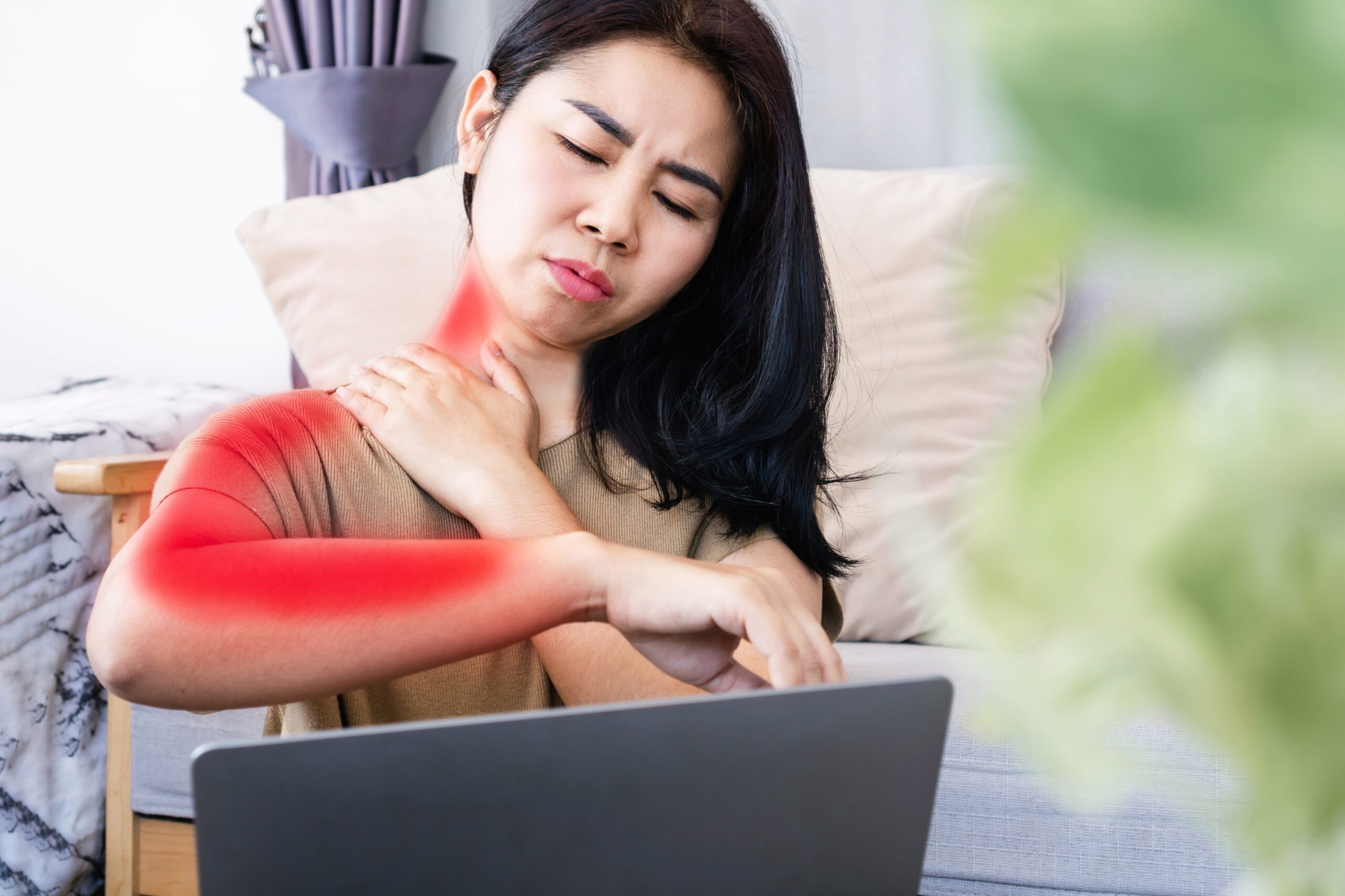 A woman working on her lap top, frustrated with neck pain and thinking about trusted cervical disc fusion surgery.