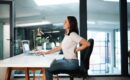 A female office employee sitting at her desk, managing back pain while she tries to work.