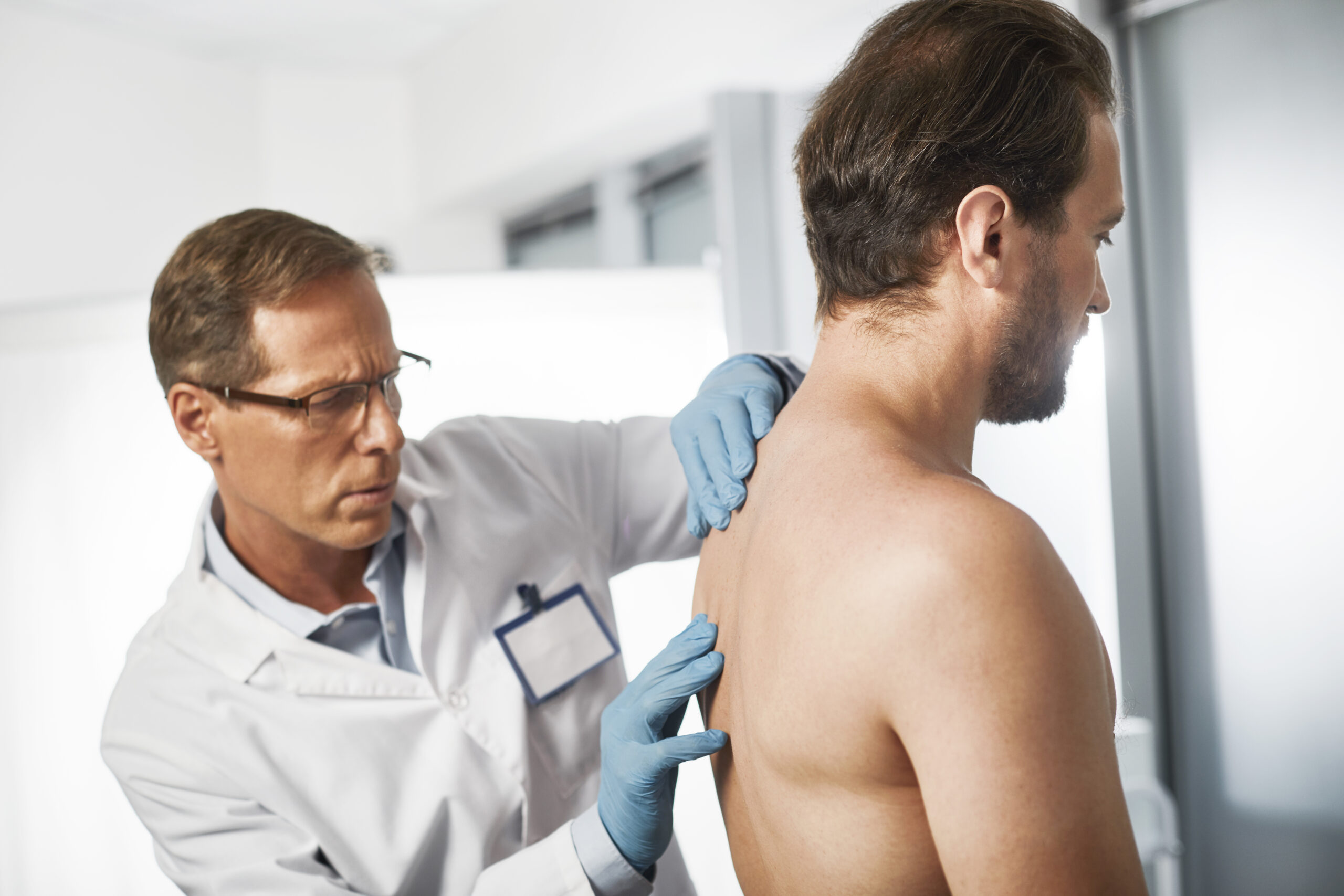 A doctor inspects a man's back during an examination, discussing specialized thoracic disc fusion procedures.