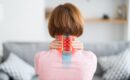 A woman sitting down, in pain, and holding her neck, thinking about specialized cervical disc fusion procedures.